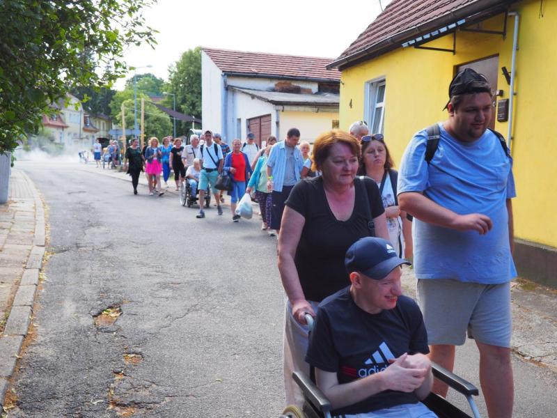 Widok ukazuje grupę uczestników, pracowników oraz rodziców Środowiskowego Domu Samopomocy, którzy spacerują ulicami urokliwego miasteczka Łagów. Atmosfera jest pełna radości, wspólnoty i pozytywnej energii.