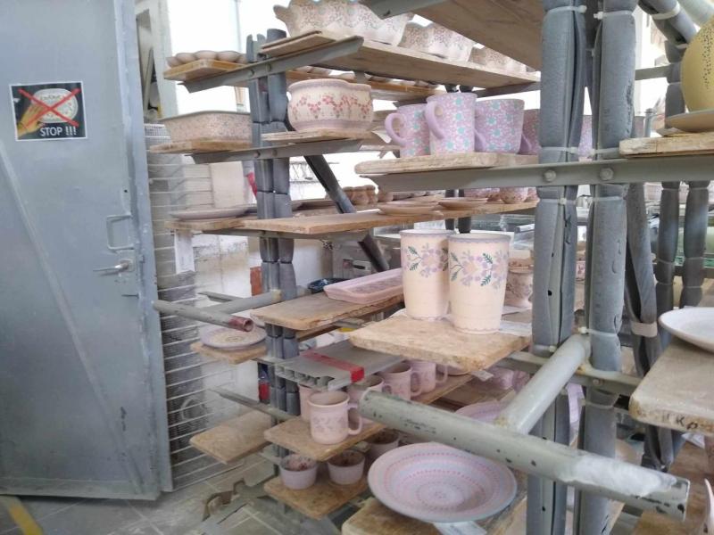 Na półkach ustawione są różne produkty ceramiczne, takie jak wazony, talerze, misy, kubki czy inne wytwory rąk rzemieślników. 